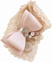Load image into Gallery viewer, A decorative hair accessory featuring a large pale pink satin bow layered over beige lace, embellished with pearl-like beads and a jeweled brooch, shown on a plain white background.