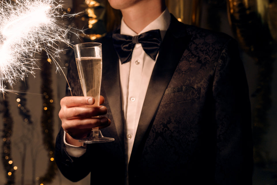 A young man wearing a black tuxedo holding a champagne glass.
